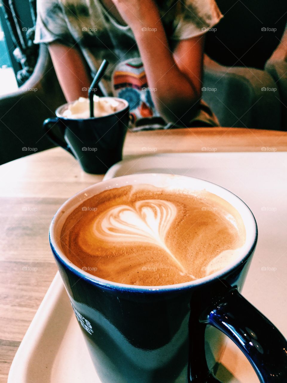 Two cups of hot drinks on the table and one person behind ,in a cafe