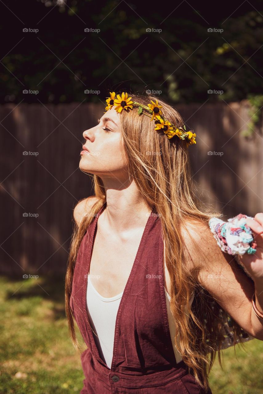 Young woman wearing a flower crown and feeling the warm sun on her face outdoors 