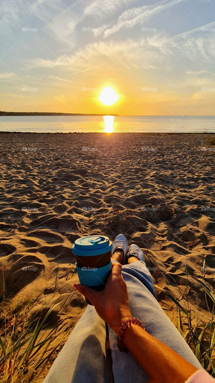 girl sitting on the sand on the beach and looking at the sunset