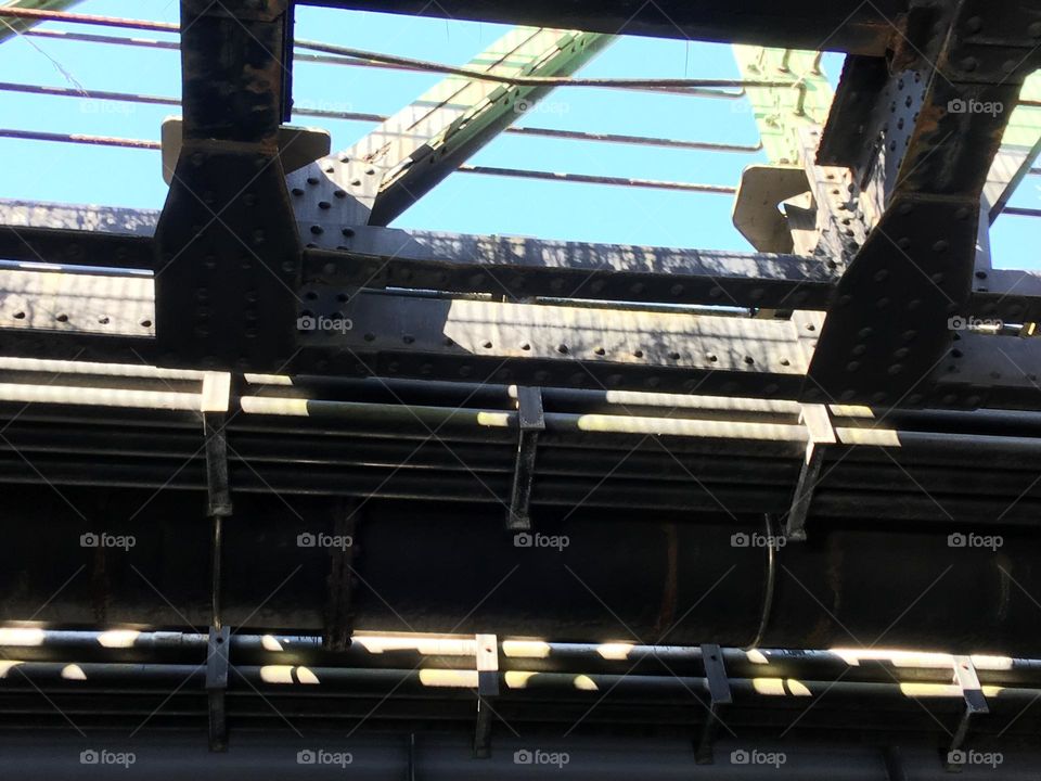 Hamburger Hafen, Brücke führt zu einem Trockendock, welche beim Durchfahren mit dem Schiff abgelichtet ist. Oberes Bilddrittel lässt durch Eisengitter den blauen Himmel erkennen, darunter viel schweres Eisen, teilweise beleuchtet durch die Sonne.