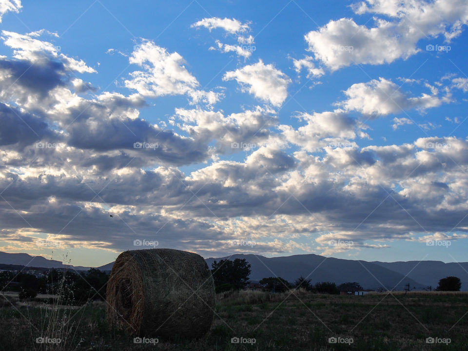 Cloudy sky over field landscape with haybale