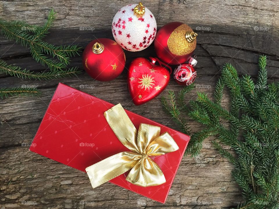 Present wrapped in red paper with golden ribbon surrounded by pine cone tree branches and red and golden globes