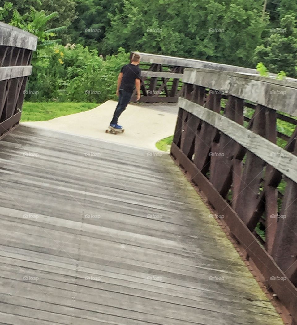 Long boarder on a bridge . A lone long boarder Rolls down a wooden bridge