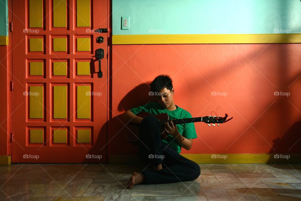 young asian teen playing guitar in a living room