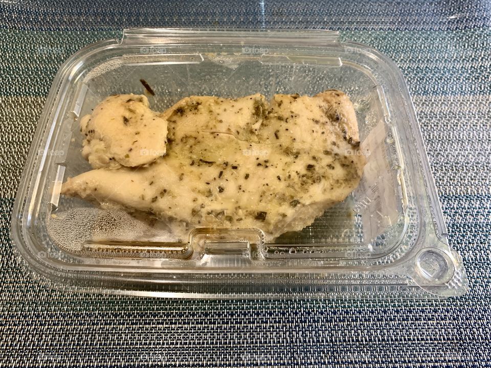 Baked chicken in a sealed transparent container with sky blue place mat background. Lunch and dinner.