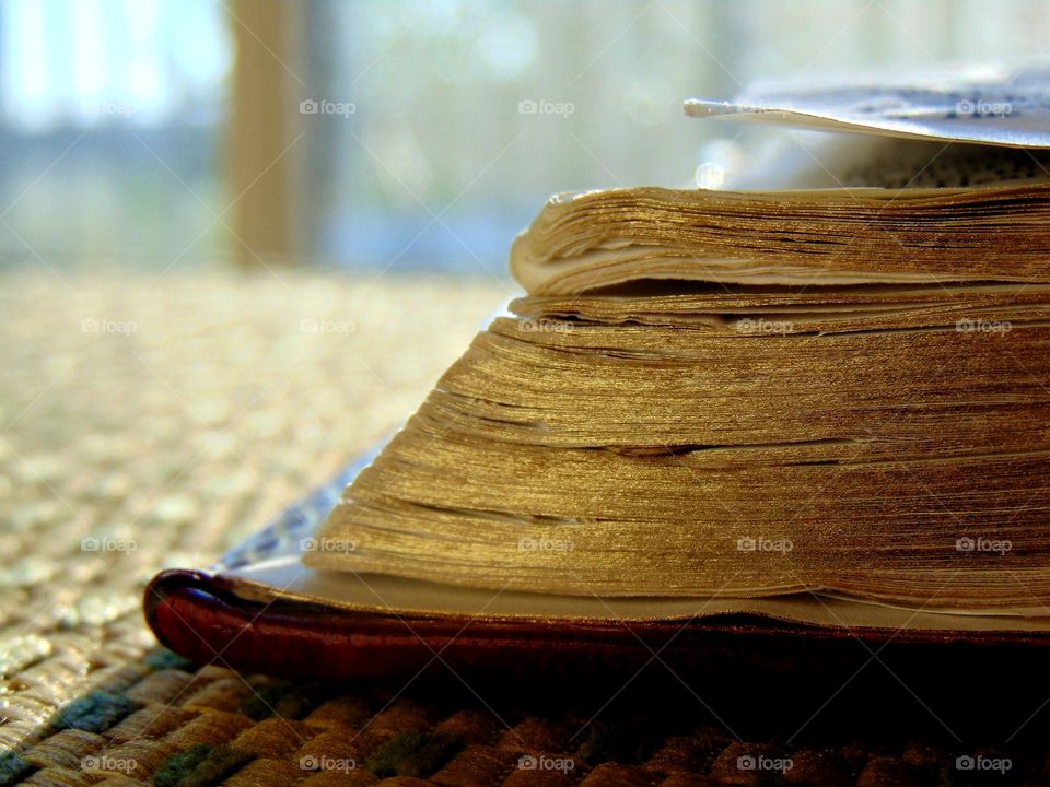 Corner edge of a book that's setting on a window seat with a window and the morning sun in the background.