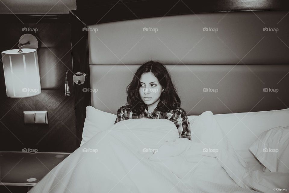 Girl lying in bed under white sheets, looks scared