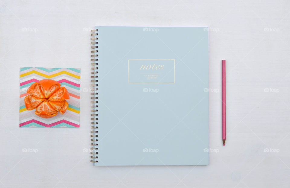 Flat lay of a notebook, orange and colored pencil