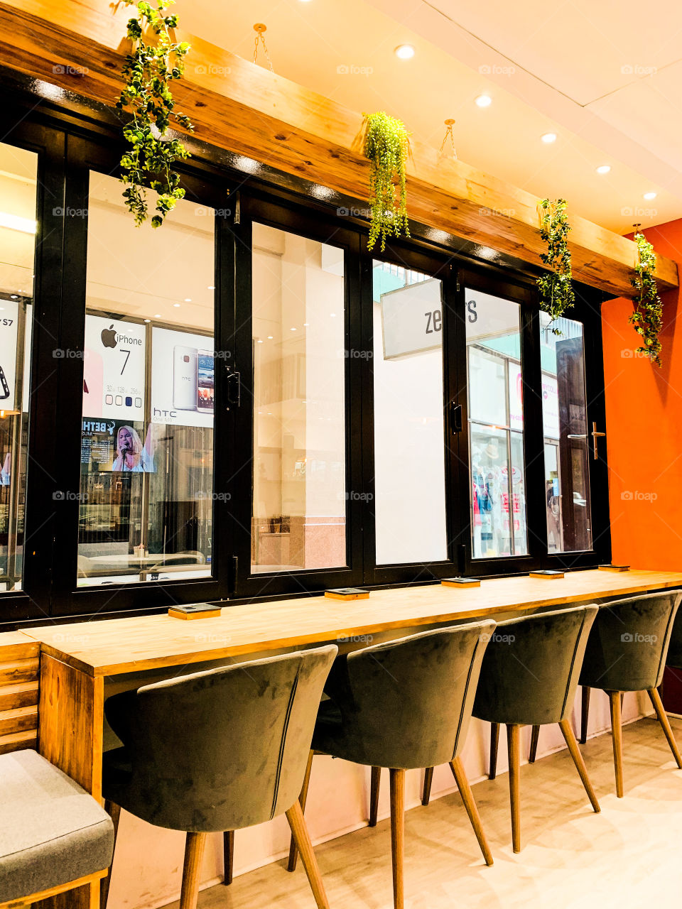 Beautiful sitting space in a coffee shop for single clients facing a glass window with green hanging plants.