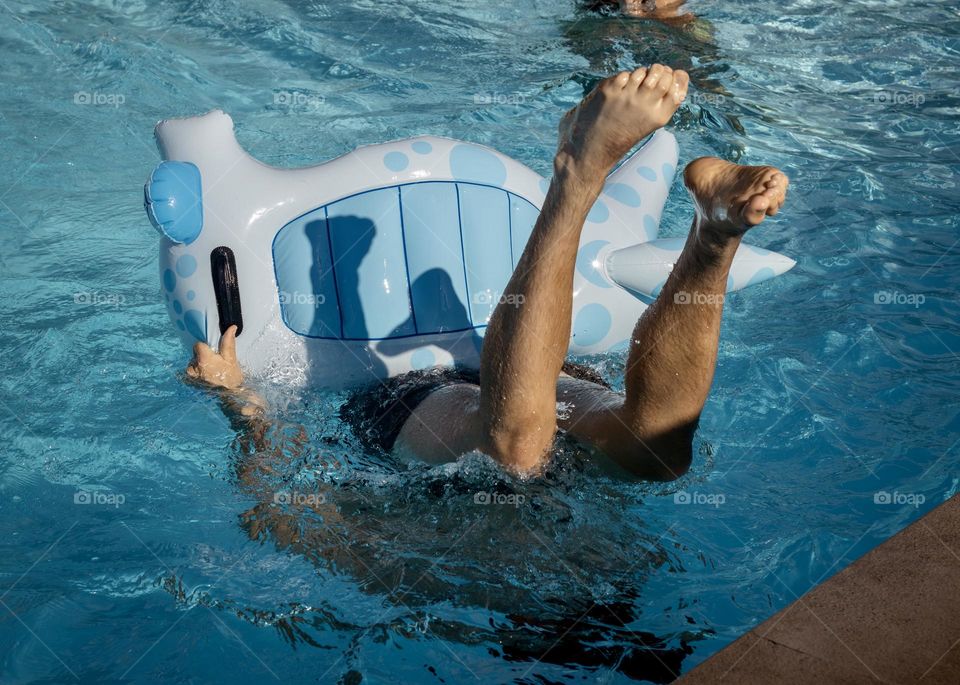 A person playing with an inflatable in the pool, goes under the water with their legs waving in the air