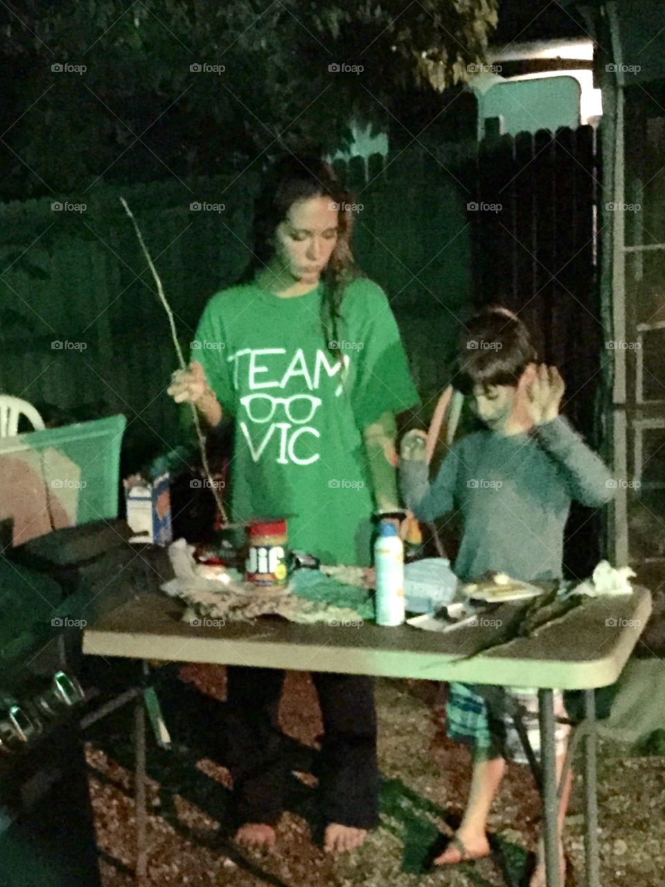 A young boy and older girl making s'mores to cook over nearby campfire.