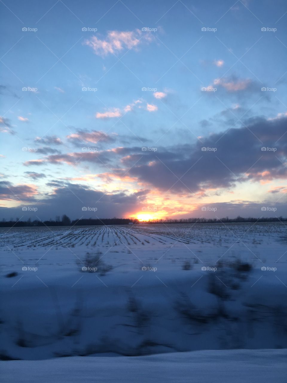 The sun sets past a snow-covered field.