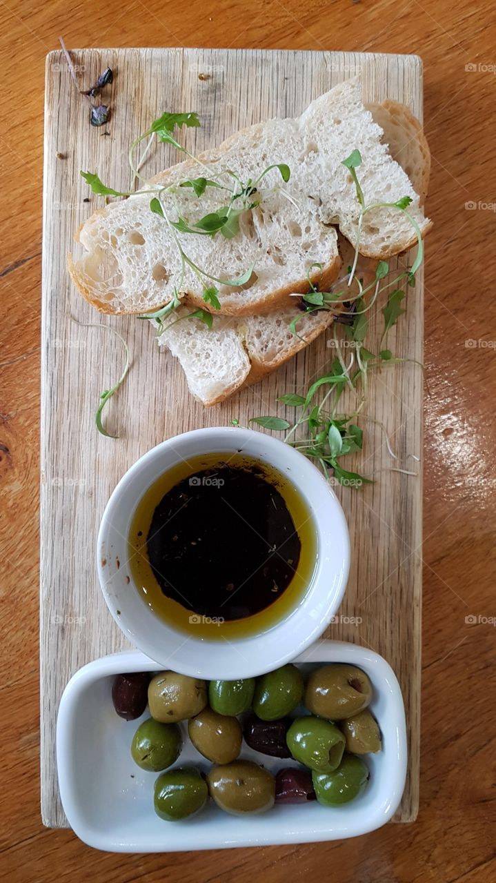 Olives, olive oil and fresh baked bread on wooden board with some green garnish