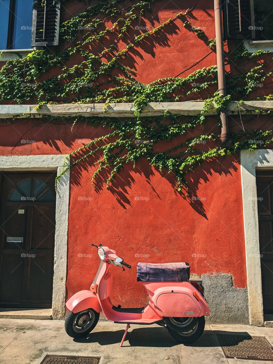 A beautiful pink Vespa motorcycle stands near red wall on the street. Transportation and city transport.