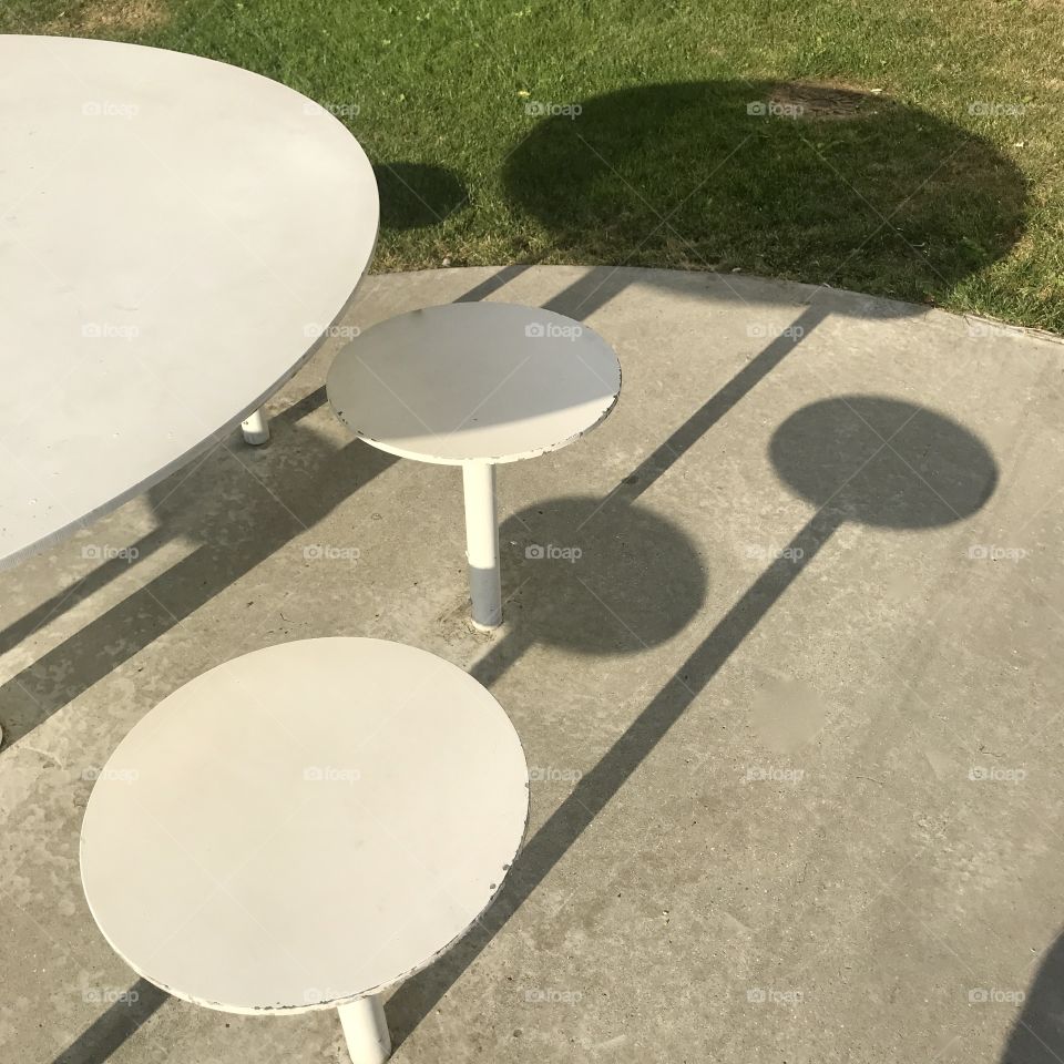 White round steel outdoor table and stools maling shadows on the concrete
