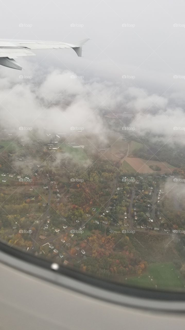 Window view from an airplane, showing homes on the ground through the clouds