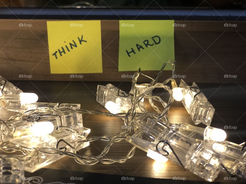Two stick notes with words’Think hard’ and some lights on a wooden table 