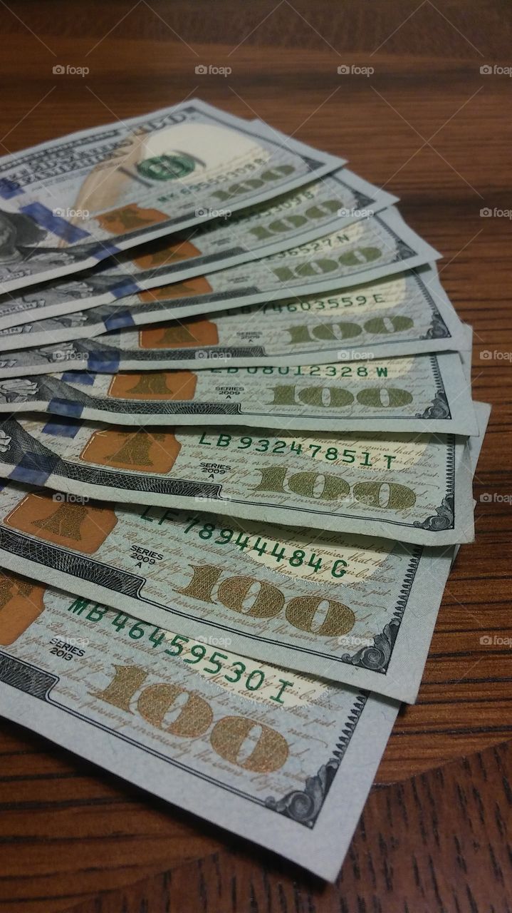 8 $100 bills fanned out on a table. ready to be spent