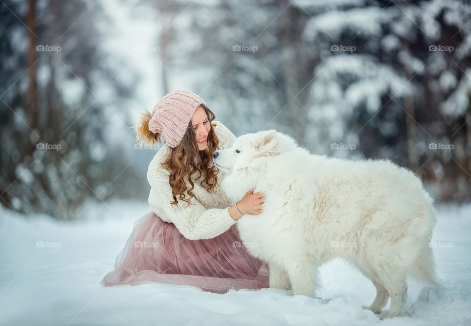 Beautiful woman with dog samoyed in winter forest