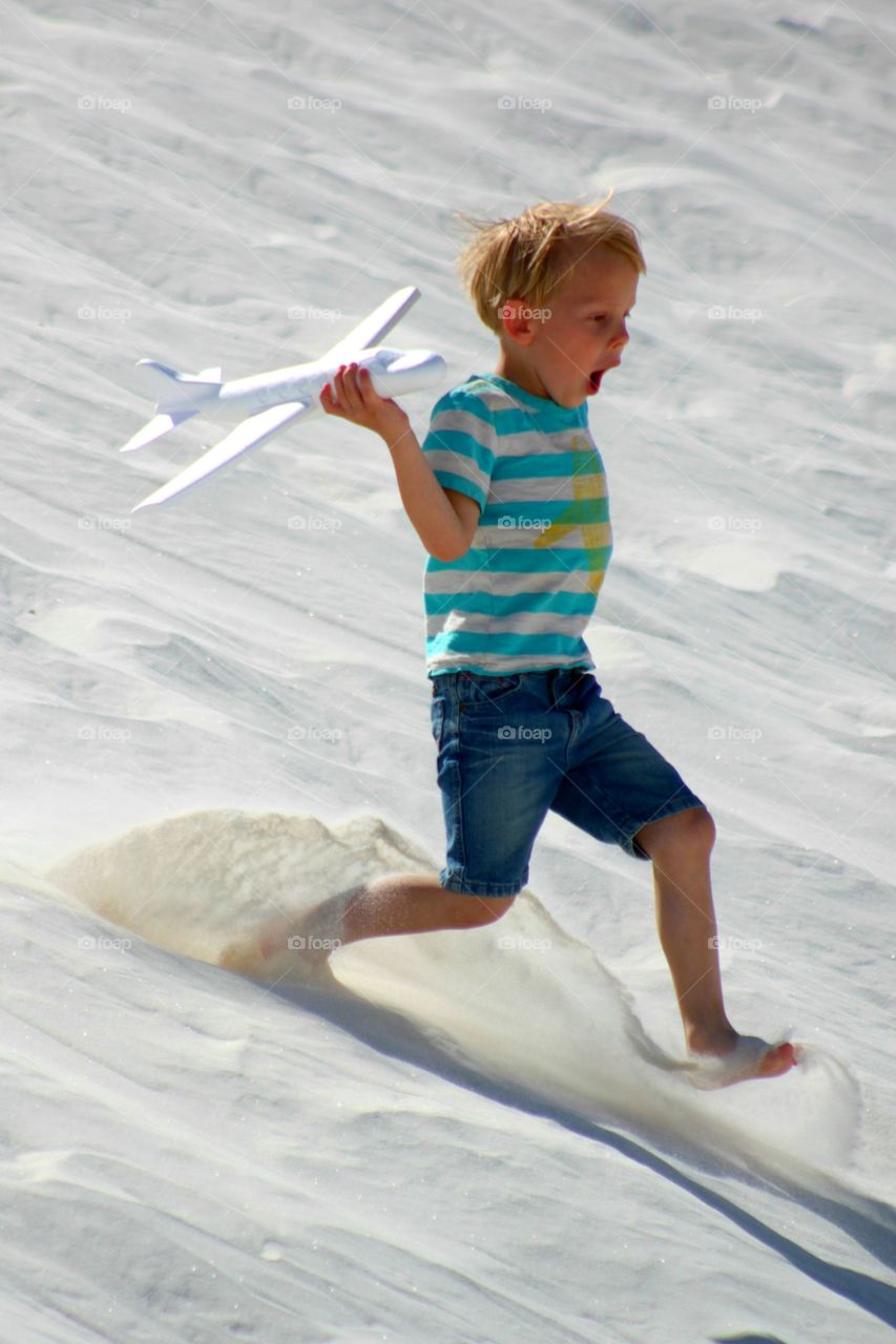 Boy playing with airplane on white sand