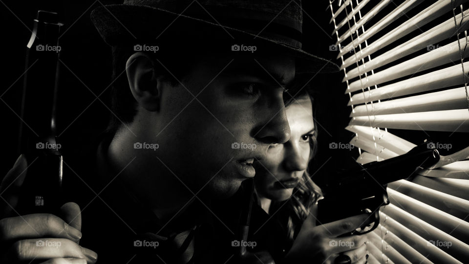 Couple with a gun standing by the window with blinds