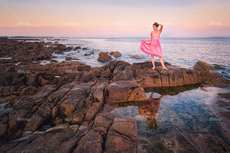 Lady in pink dress reflected in water standing by the ocean