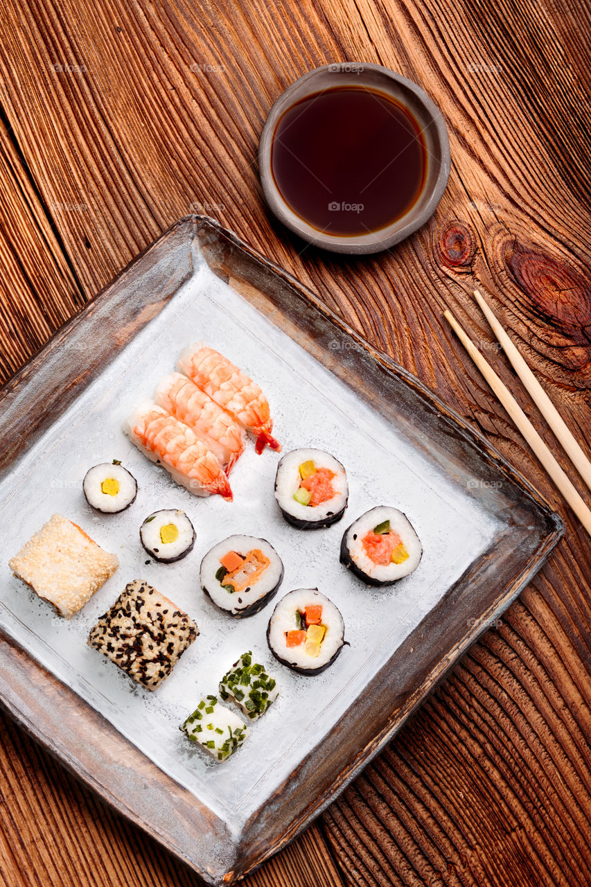 Sushi set on pottery plate with chopsticks and soy sauce in bowl on old wooden table from above