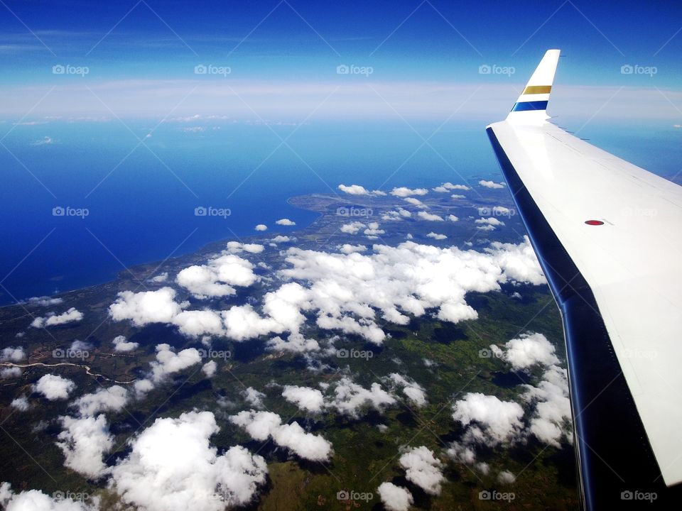 airplane wing, sky, clouds, ocean and an island