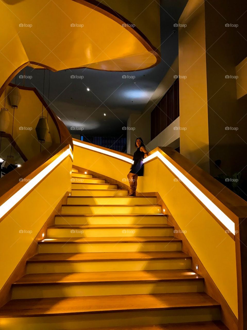 a girl was standing at the stair, with the stairway light shining in yellow