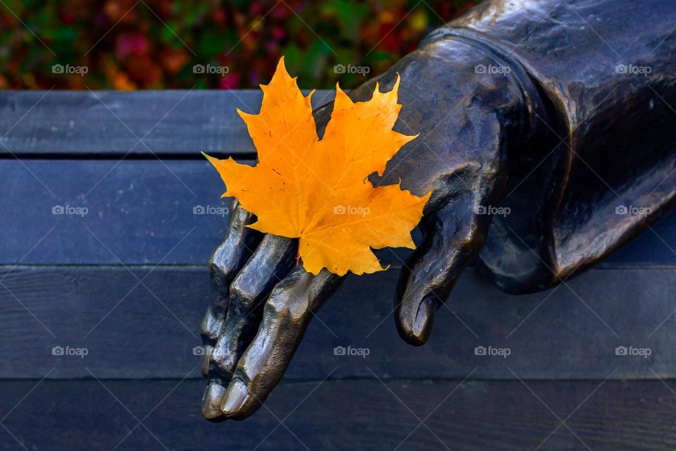 city statue made of metal in the park, autumn yellow maple leaf on hand