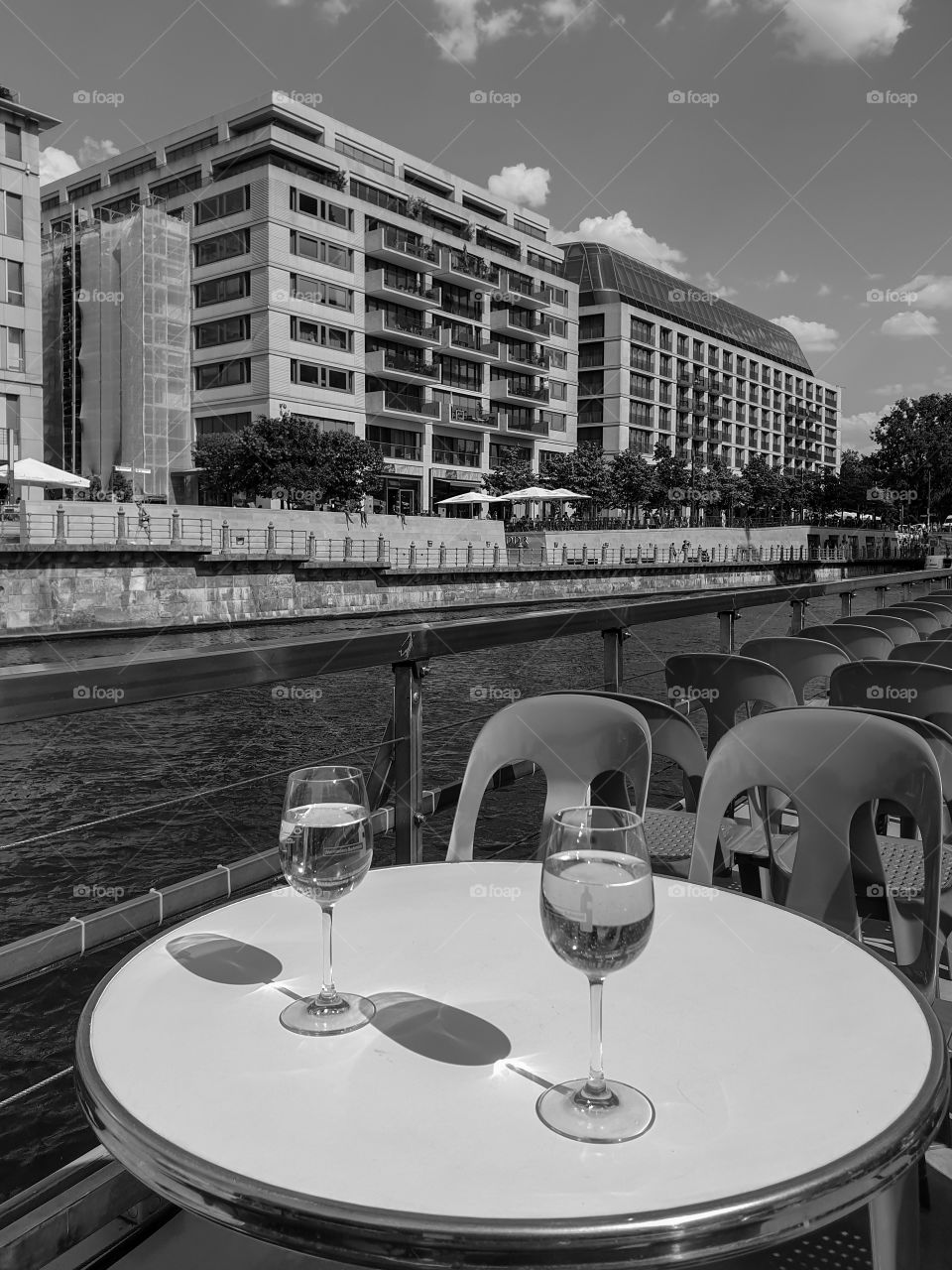View from the pleasure river ship to the modern houses of the center of Berlin. Monochrome cityscape with a pleasure boat with two glasses of white wine on the round table