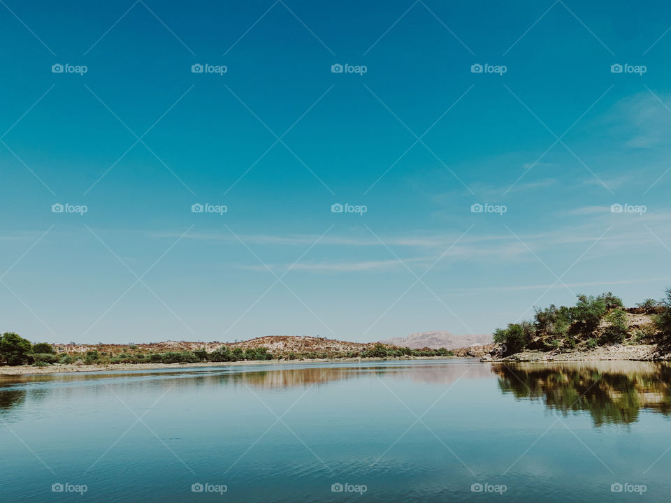 A beautiful blue snap of the sky reflecting in the lake water with mountains and hills on the shore.