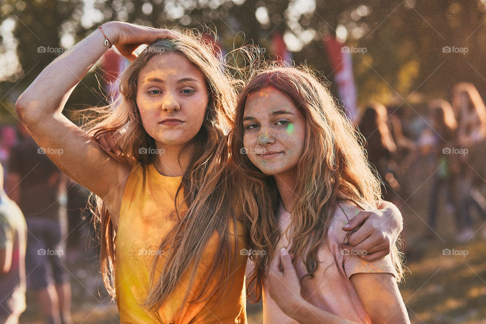 Portrait of happy smiling young girls with colorful paints on faces and clothes. Two friends spending time on holi color festival. Real people, authentic situations