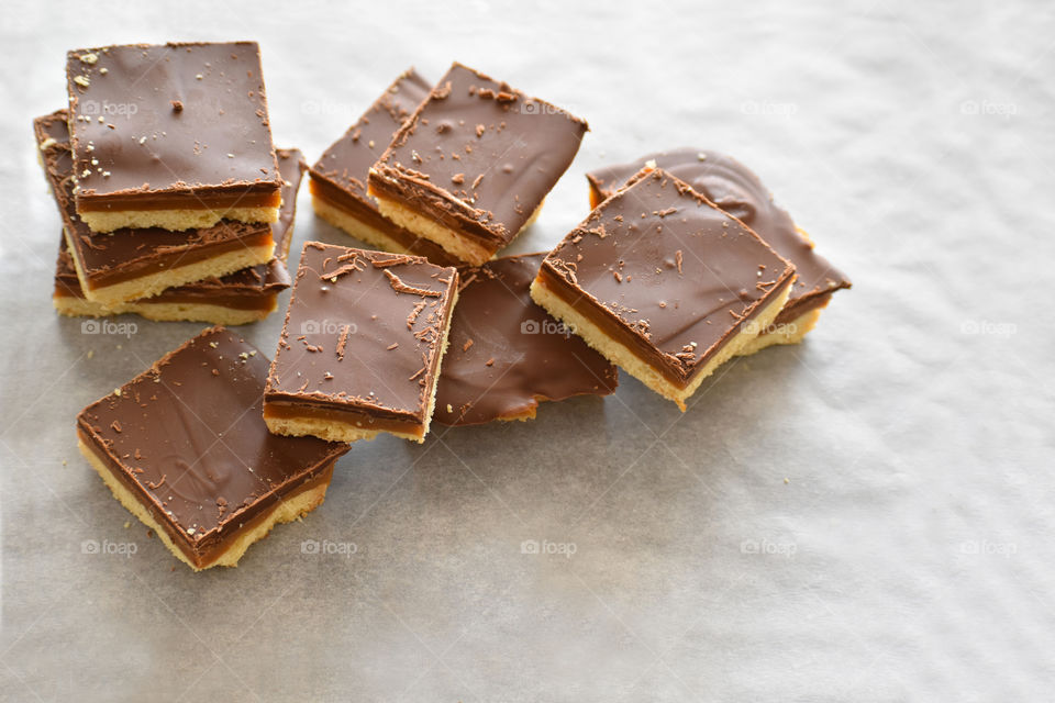 Millionaire's shortbread with chocolate and caramel on a parchment paper with copy space on the right bottom side.