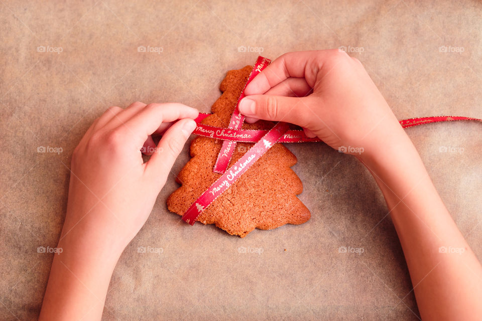 Girl tying baked Christmas gingerbread cookies with ribbon