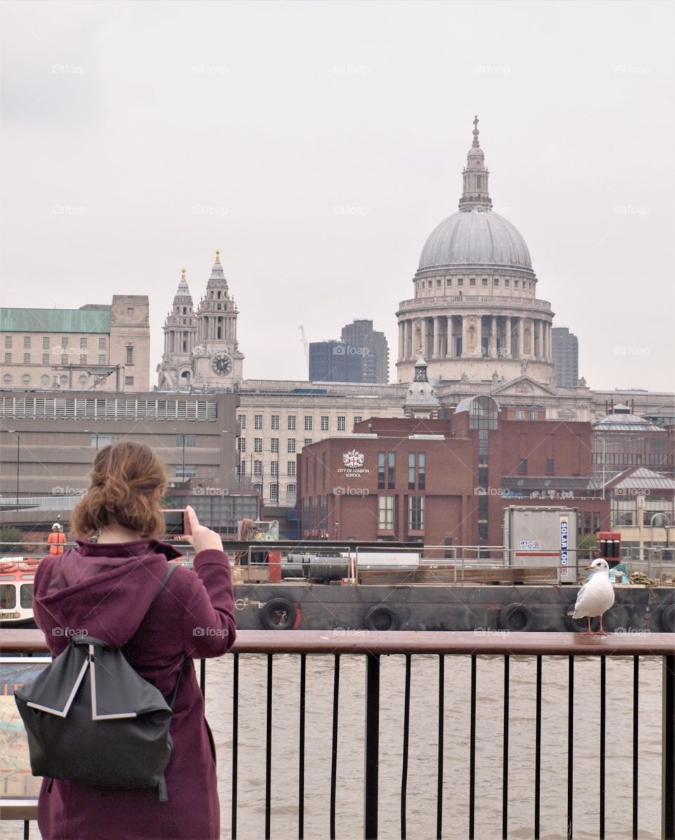 A young woman taking a photo of St Paul's Cathedral with her phone