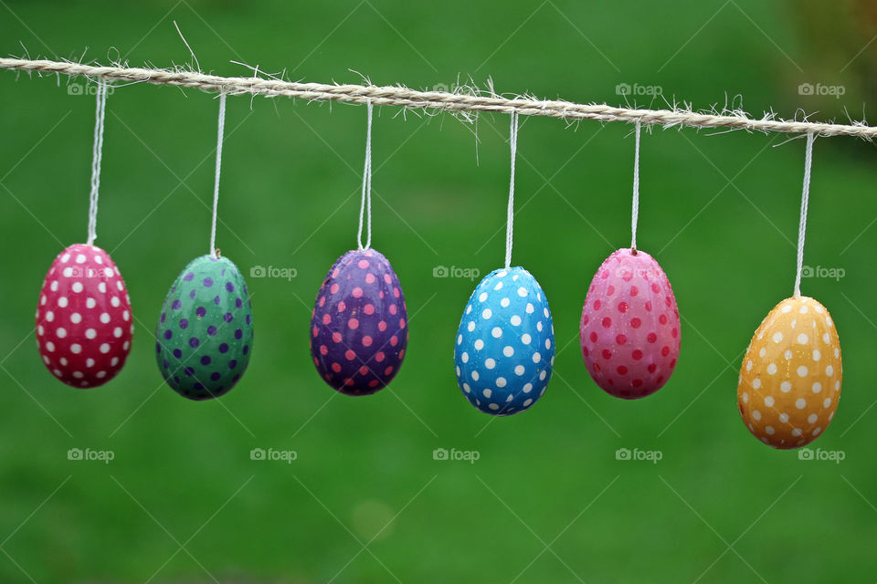 Colorful,  painted polkadott eastereggs hanging on a rope with green background