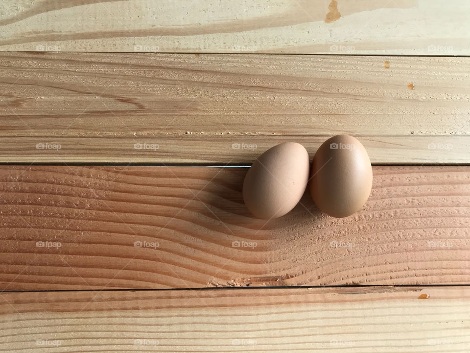 top view of two fresh organic chicken eggs on natural rubber wood board table with copy space on left side of frame