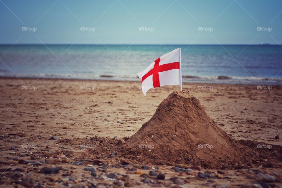 A sandcastle on a Great British beach with an English Flag and the ocean behind.