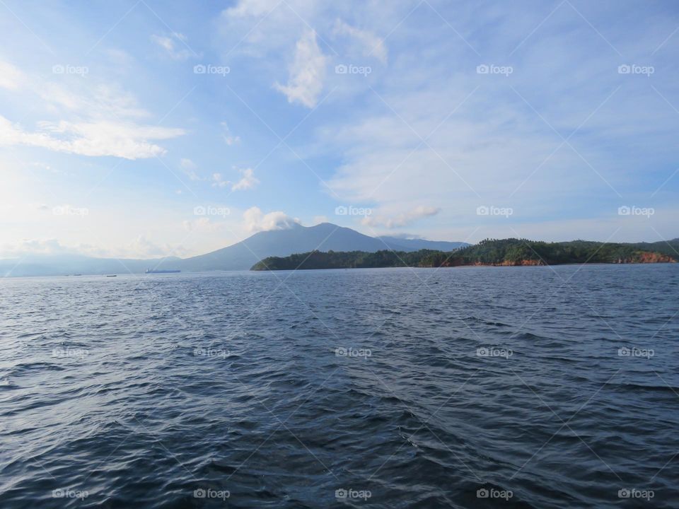 Natural view from the sea, view of green hills against the backdrop of mountains and beautiful cloud formations.