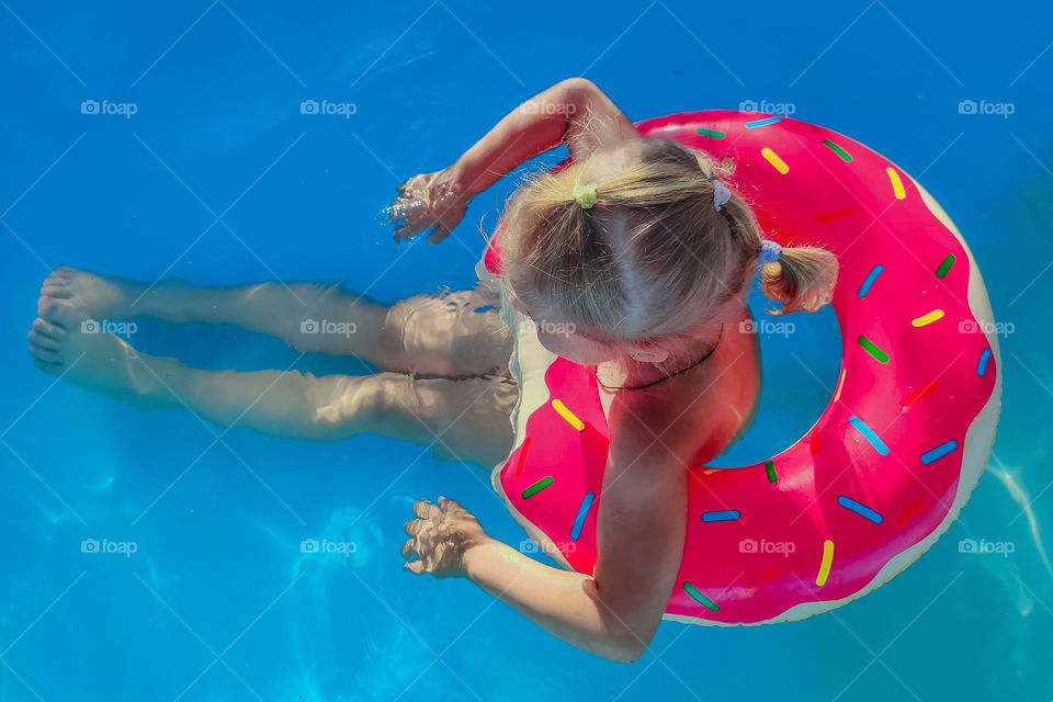 little girl swims in the pool on a pink inflatable circle