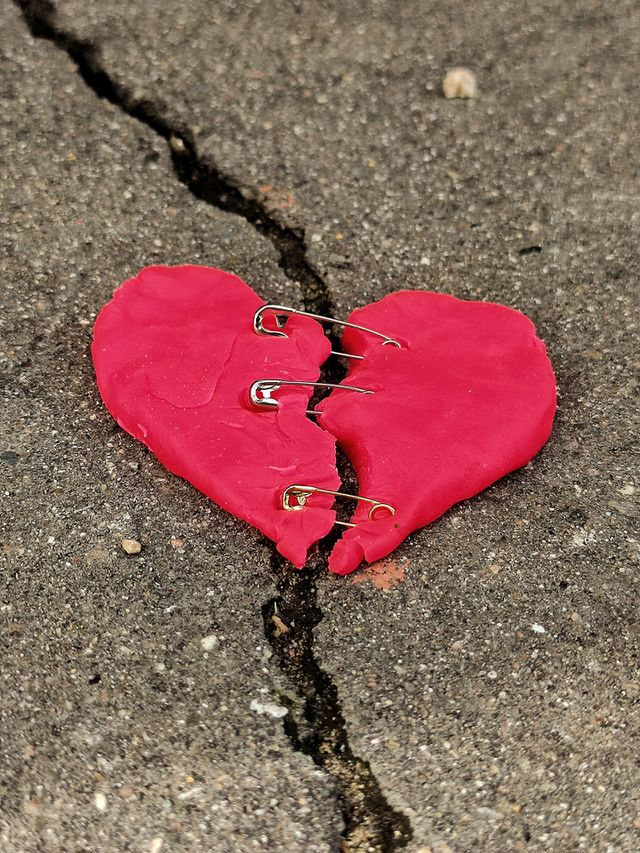red "torn" heart held together by metal pins, which lies on the cracked asphalt