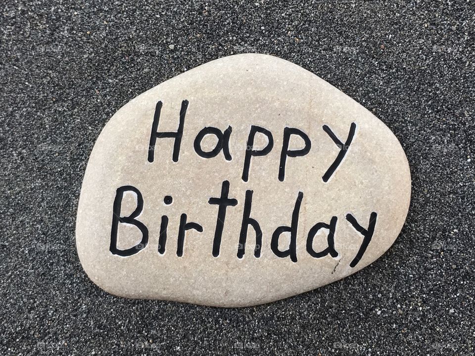 Happy Birthday text carved on a stone with black volcanic sand background