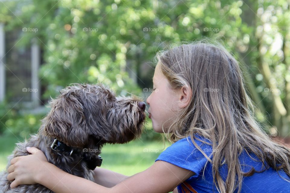 Little girl face to face with dog that is unsure if he wants a kiss 