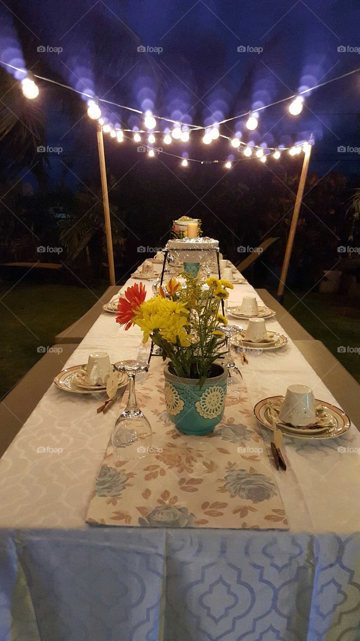 Long table set for evening tea party with  white table cloth and flowers.