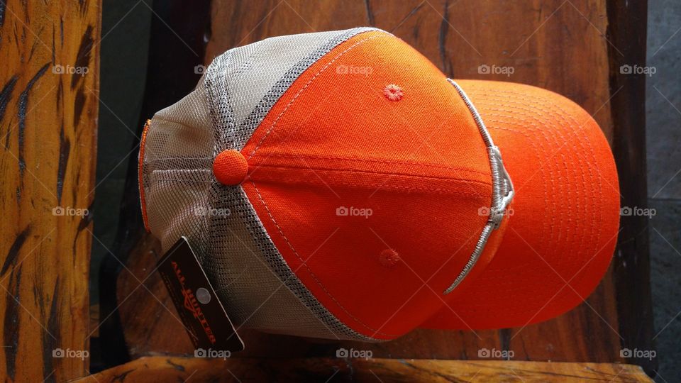 Lindo boné country, nas cores laranja e prata. Num banco de madeira.