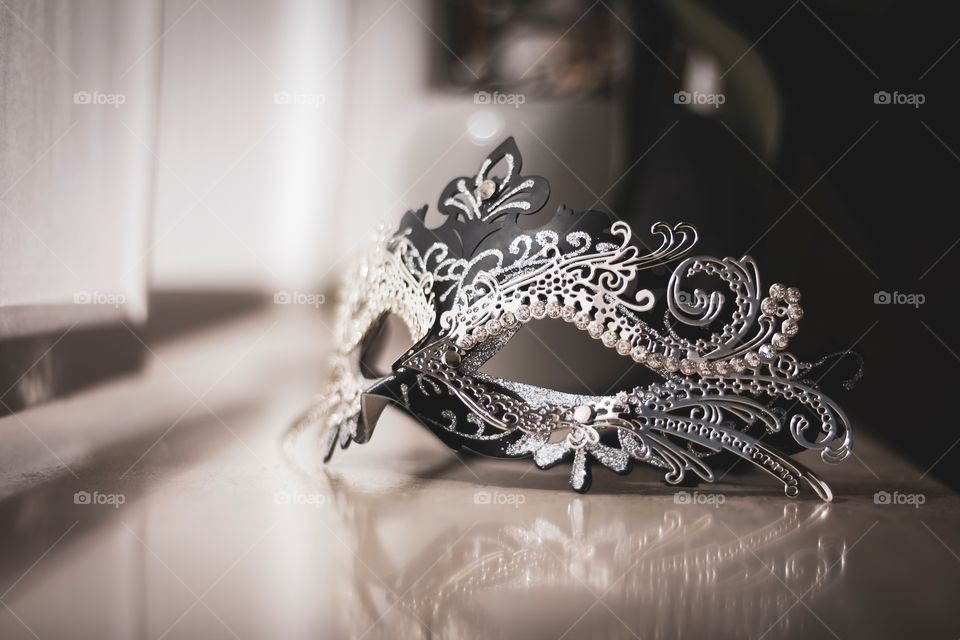 A mysterious venetian mask on a windowsill ready to be put on to hide someones identity at a masked ball.