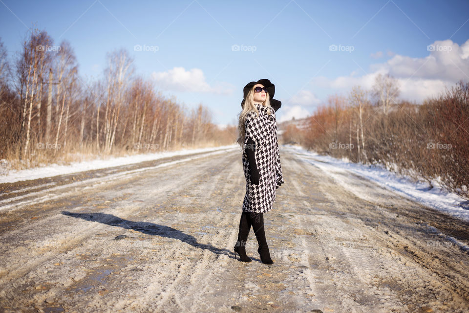 Fashionable blonde woman standing on road during winter