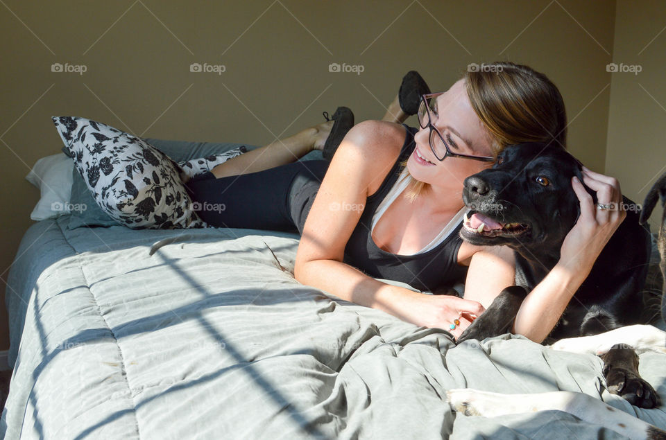 Woman laying on a bed while snuggling with her pet dog