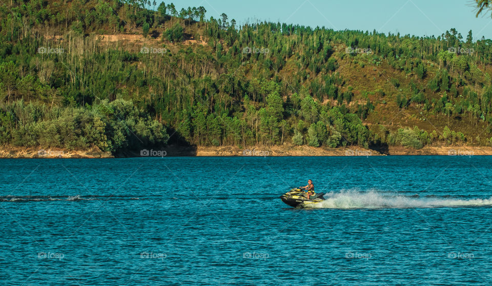 A man rides his jet sky on a calm blue river with green hills behind him